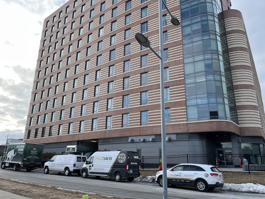 Exterior of UMASS Boston's East Residence Hall during the day with Paul Davis vehicles parked outside
