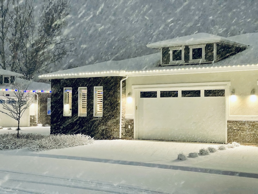 A home with holiday lights in a neighborhood during a snowstorm.
